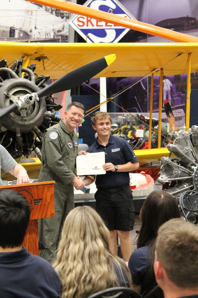 A military pilot presenting an aviation certificate to student Greyson Waller.