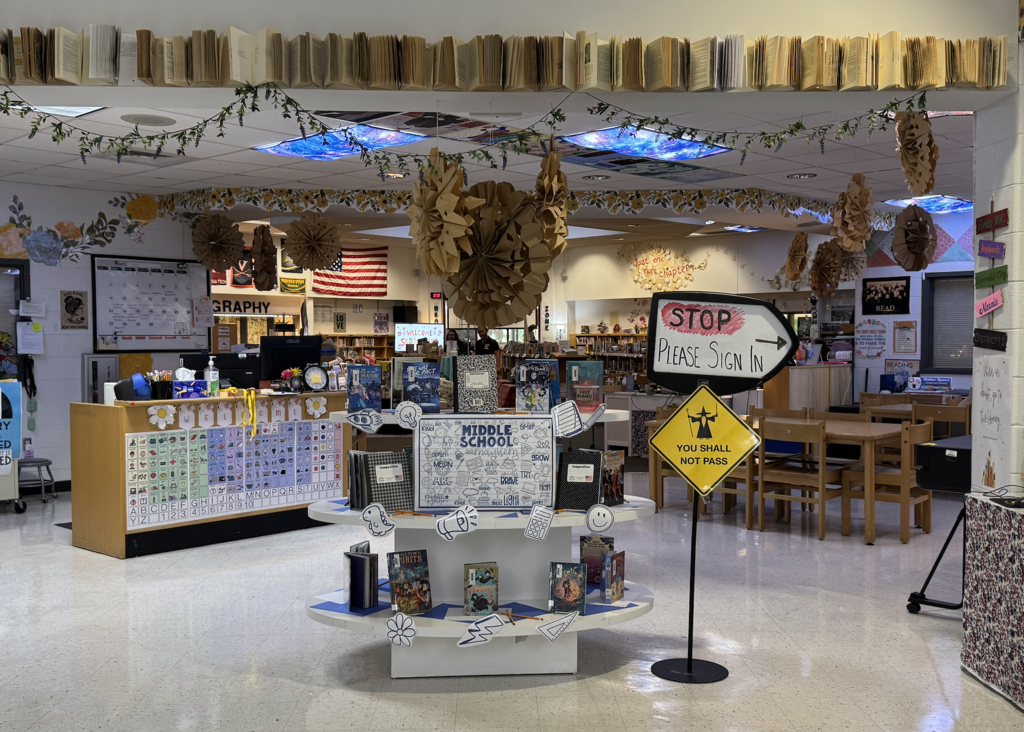 A middle school library display features books arranged on tiered white stands.