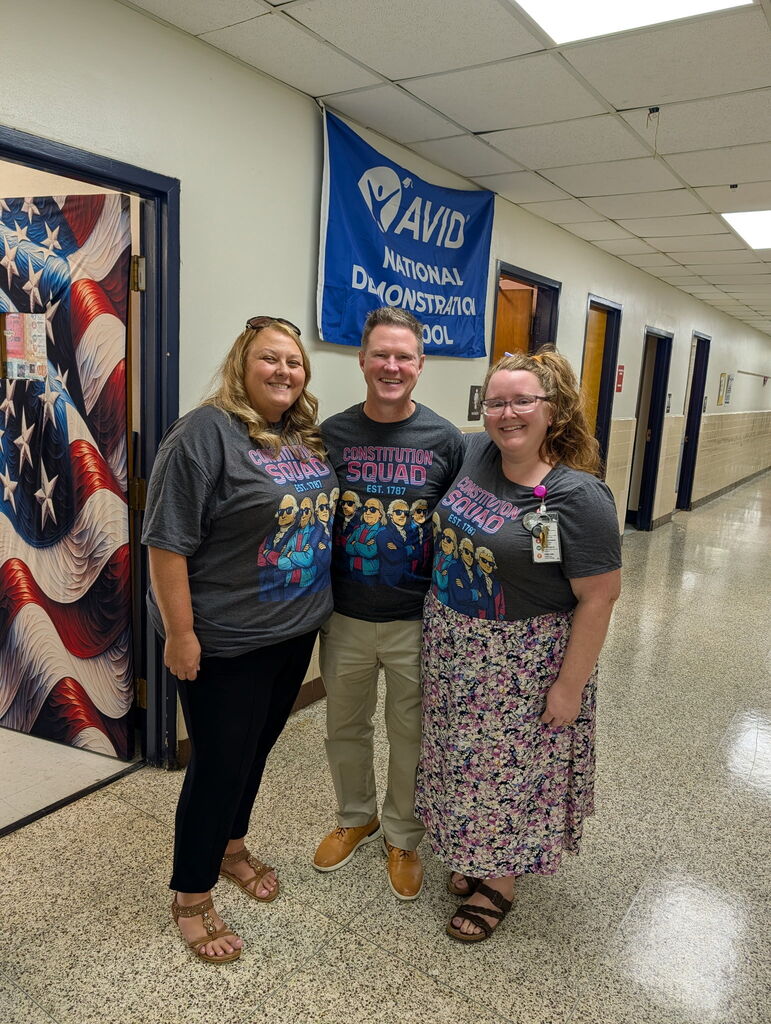 Three 7th grade History teachers stand together in a school hallway, smiling and wearing matching gray “Constitution Squad — Est. 1787” T-shirts in celebration of Constitution Day.