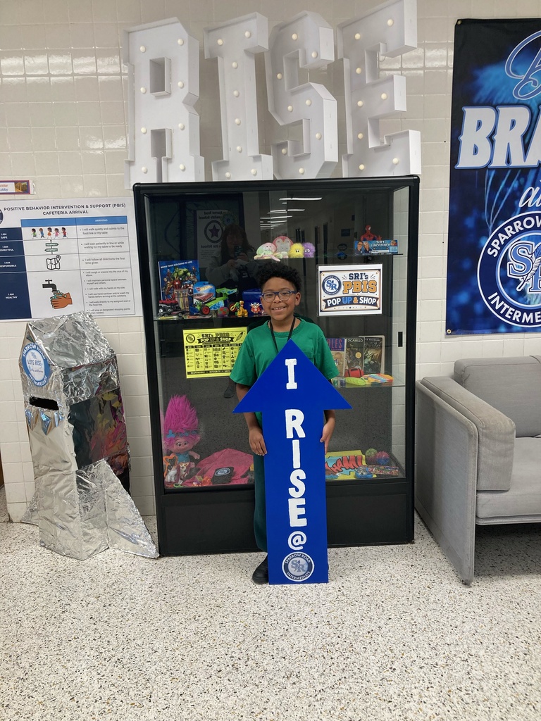 Student holding up the "I RISE" sign in the main lobby.