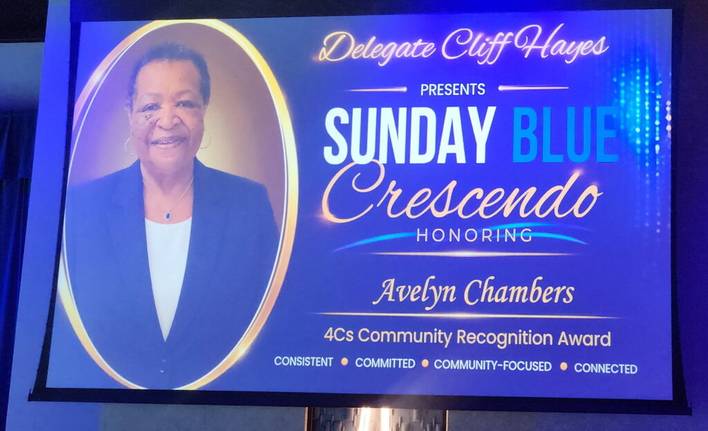 A projected presentation slide on a blue background. On the left, an oval frame contains a portrait of a smiling Black woman in a blue blazer. On the right, gold and white text reads: "Delegate Cliff Hayes presents Sunday Blue Crescendo Honoring Avelyn Chambers, 4Cs Community Recognition Award."