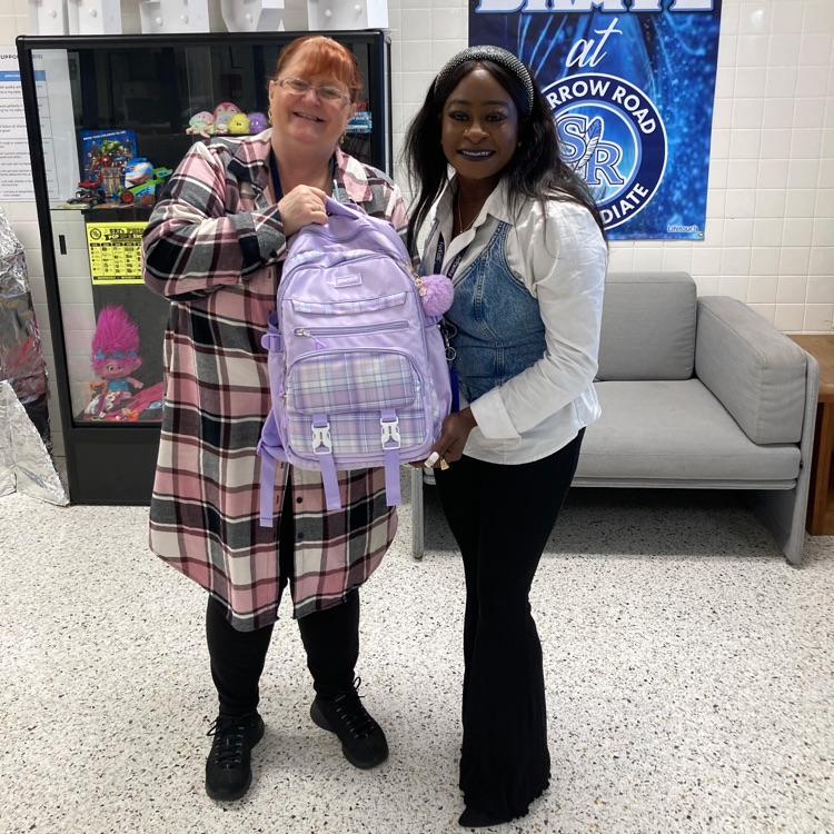 Two adults holding up a backpack in the main lobby of the school. 