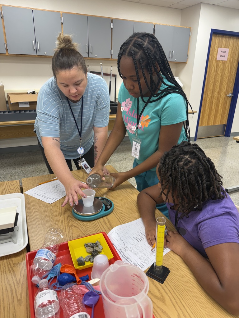 Teacher helping students pour water into a cup on a scale.