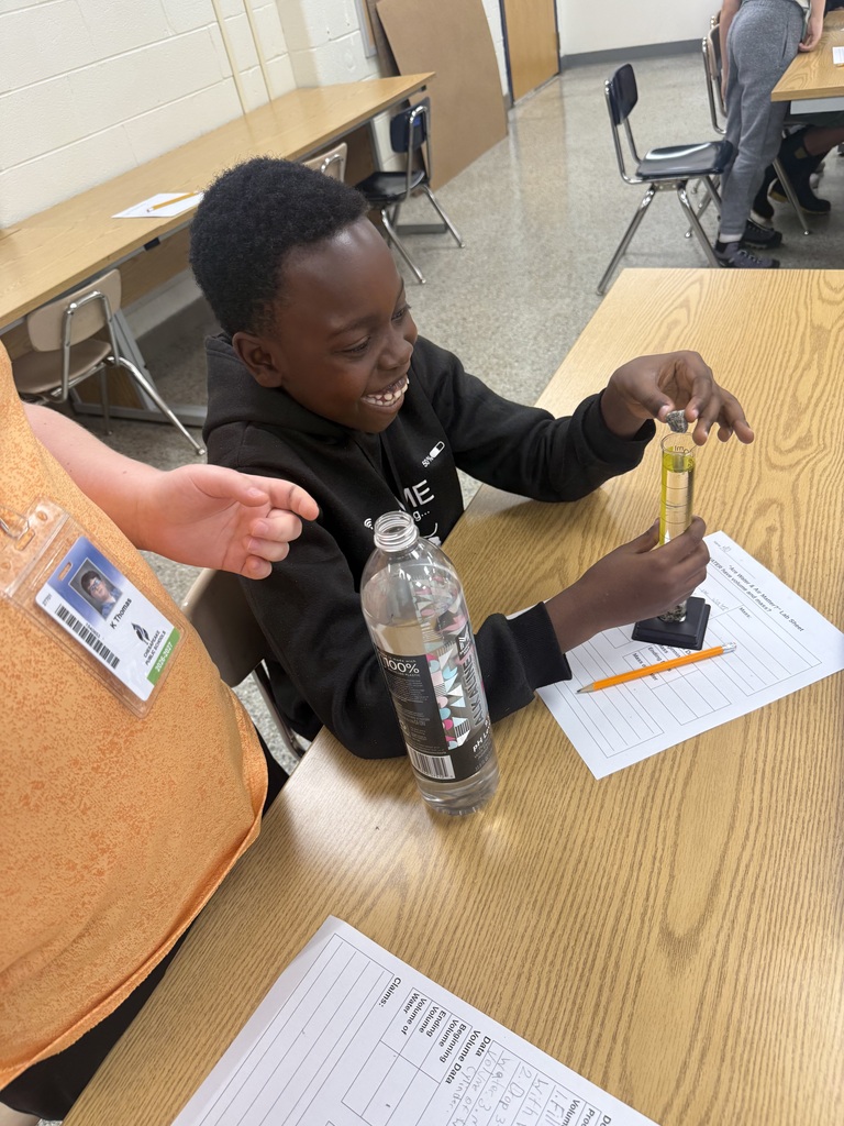 Student smiling and putting a rock into a graduated cylinder.