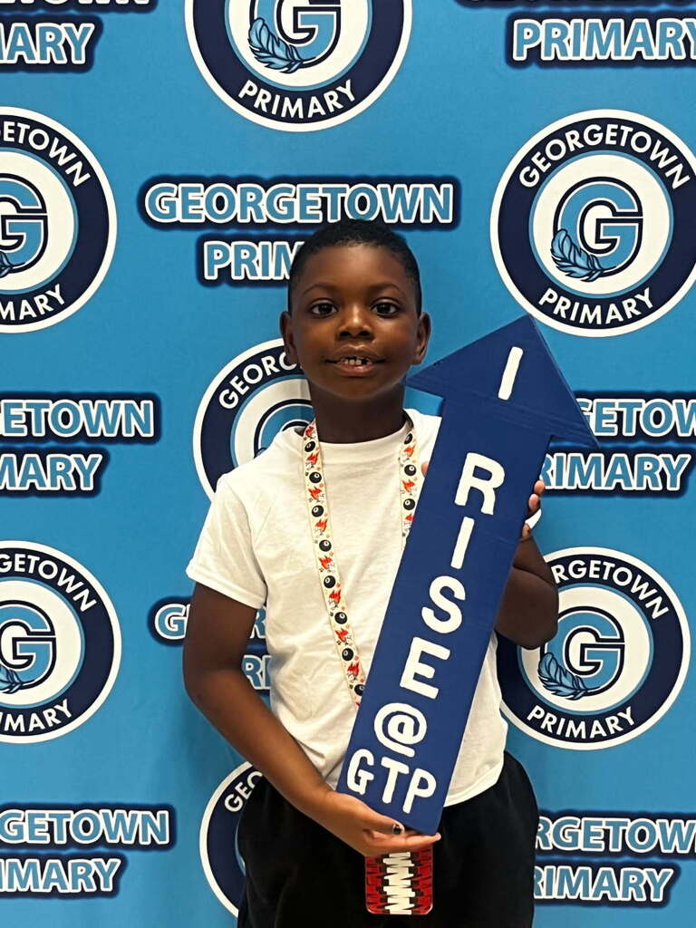 male student poses in front of Georgetown Primary backdrop with the RISE arrow