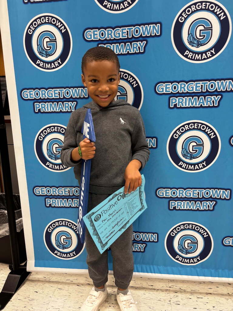 male student poses in front of Georgetown Primary backdrop with the RISE arrow