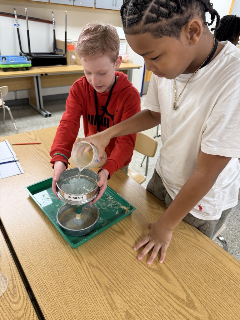 Two students in the science lab pouring a mixture into a sieve.