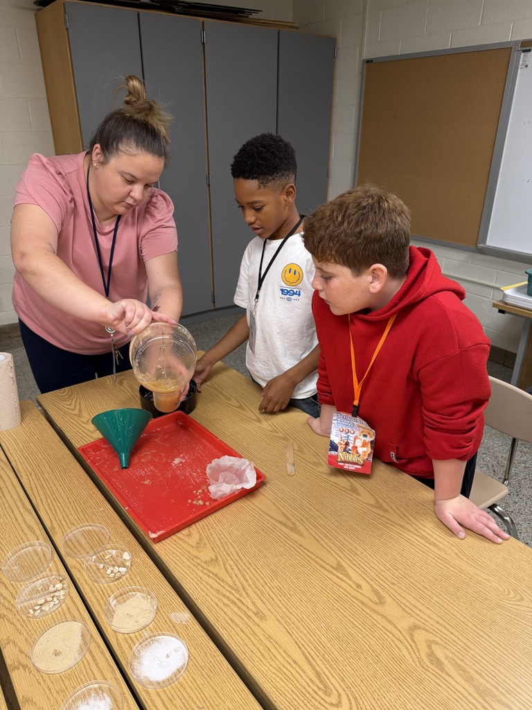 Two students and a staff member in the science lab pouring a mixture into a sieve.