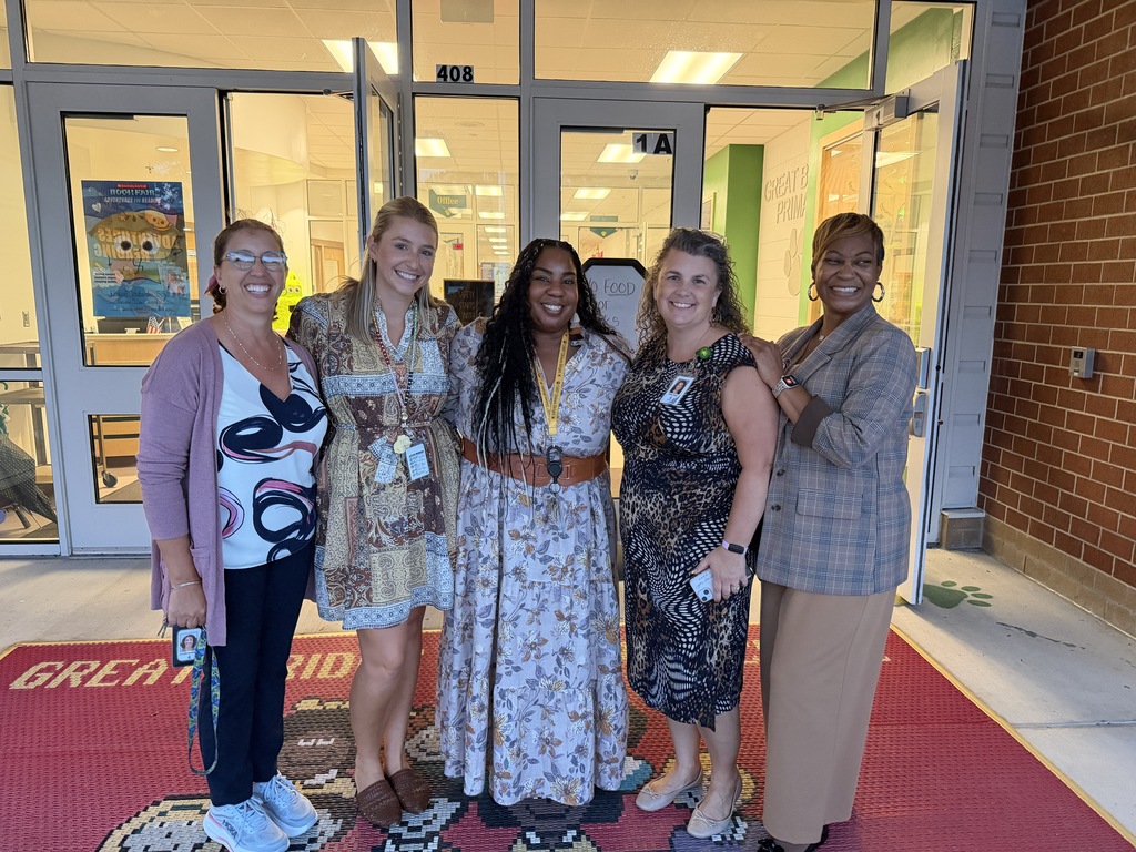 A group of staff members standing together excitedly waiting to welcome families in the building for Open House.