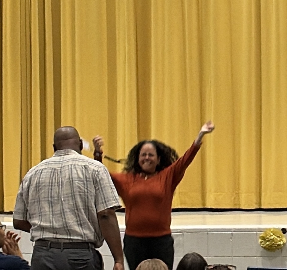 A photo of a female adult in a red shirt congratulating a male in a white plaid shirt.