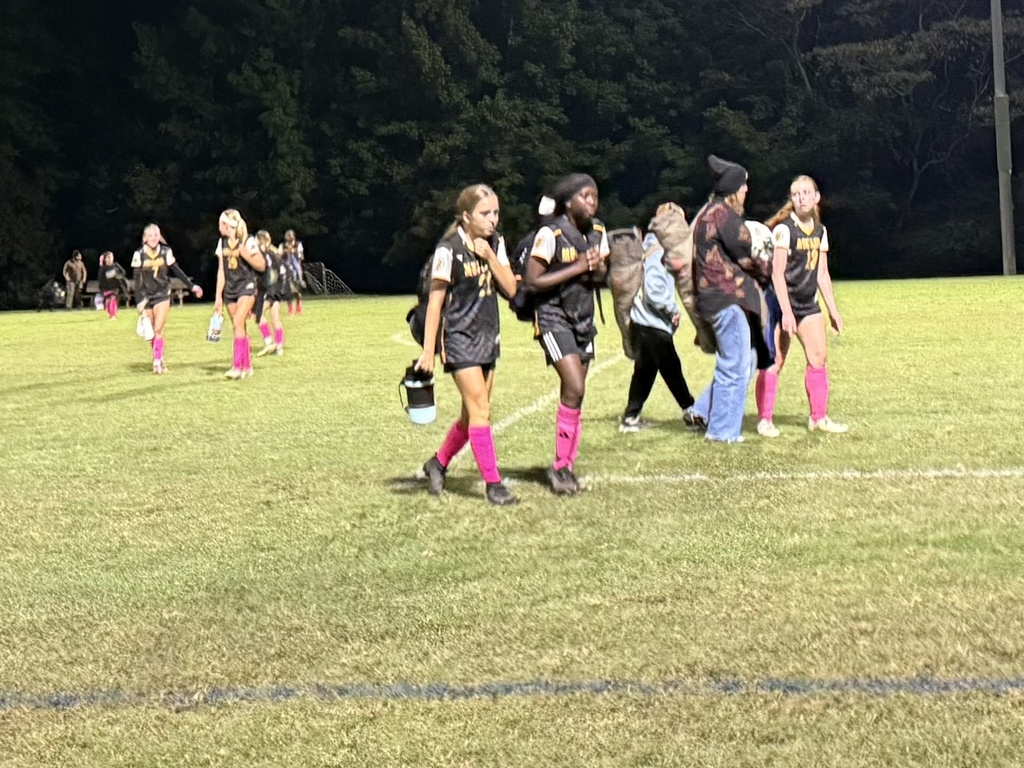 A group of students walking on a soccer field after a game.  They are carrying bags and water bottles. 