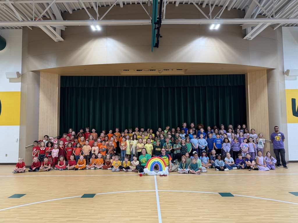 Students at Great Bridge Primary line up by color to form a large rainbow, creating a colorful display of school spirit on the school grounds.