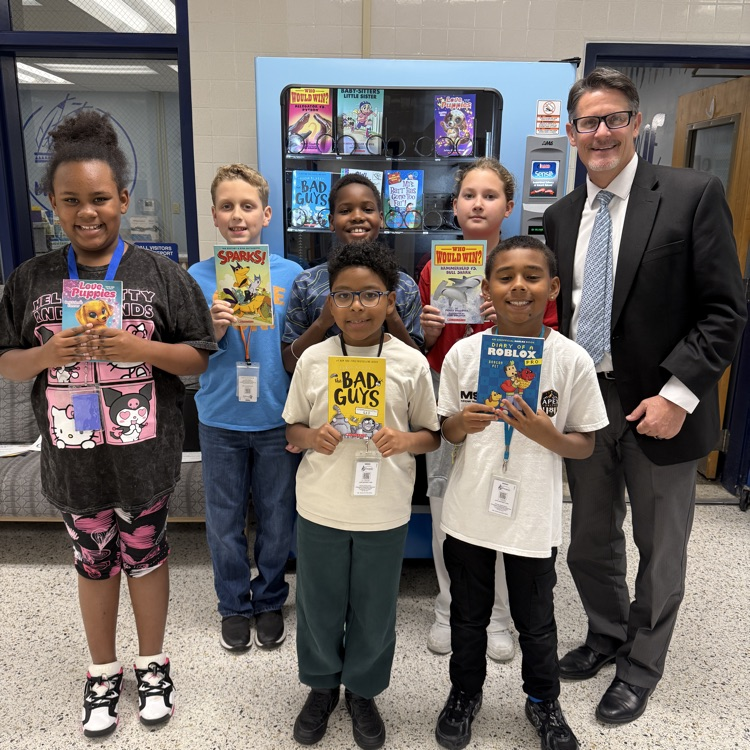 group of students holding up books with Mr. Triolet in front of book vending machine.