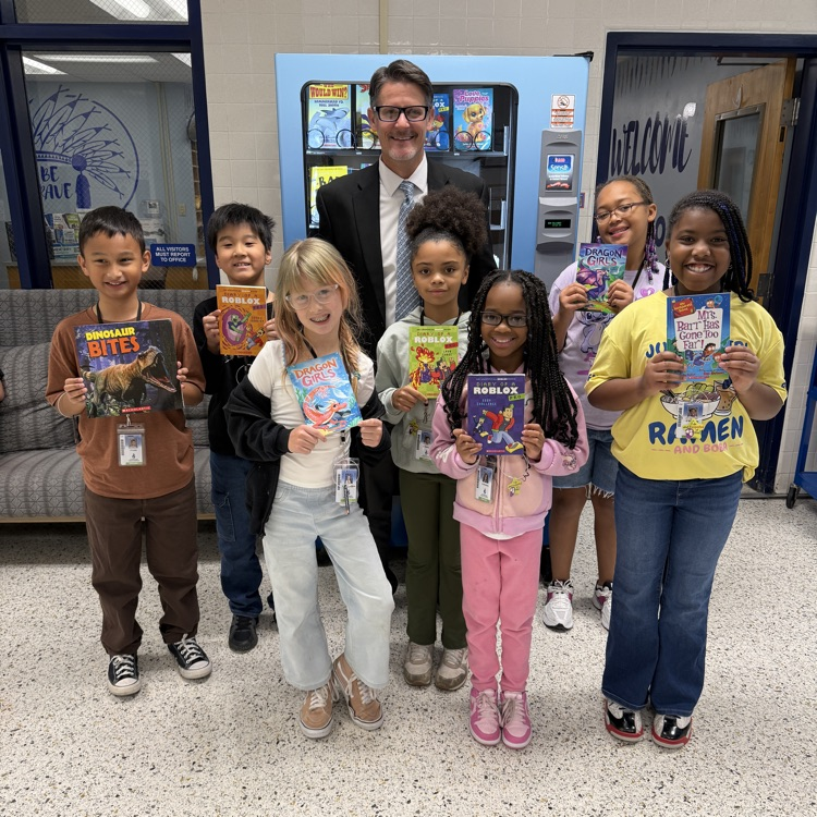 group of students holding up books with Mr. Triolet in front of book vending machine.