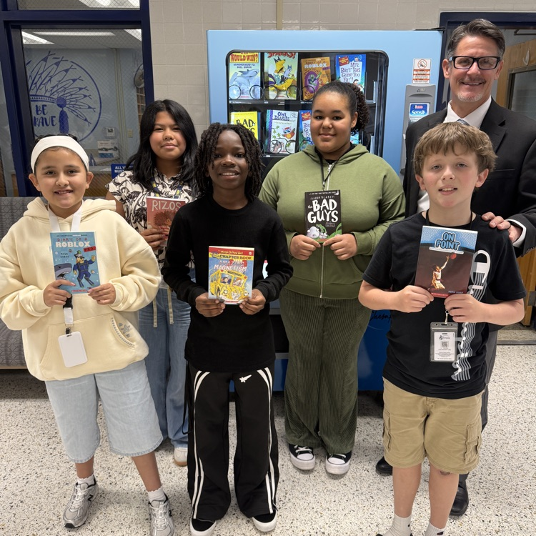 group of students holding up books with Mr. Triolet in front of book vending machine.