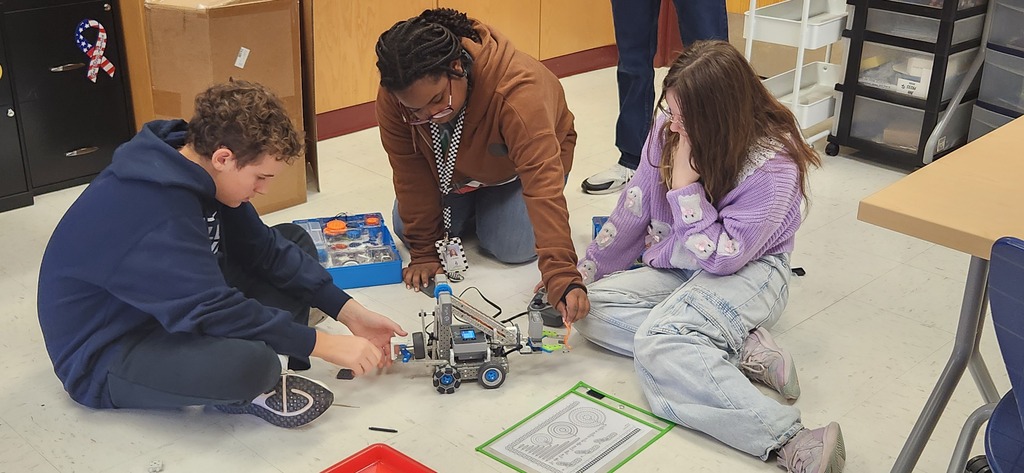 3 students working to adjust the parts of their robot
