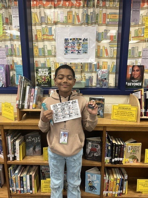 Student holding up their completed Genre Bingo Challenge Card and prize.