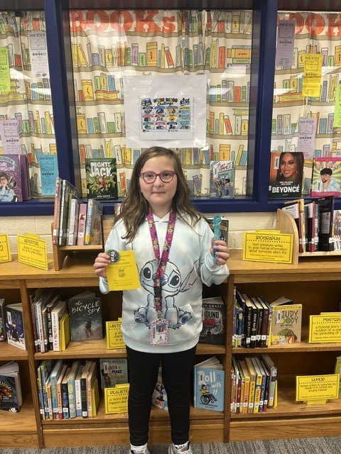 Student holding up their completed Genre Bingo Challenge Card and prize.