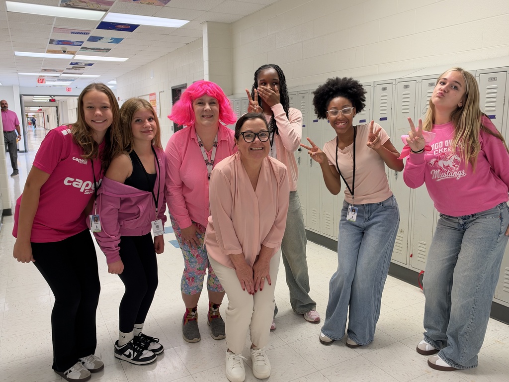 A group of people standing in a hallway wearing various shades of pink.