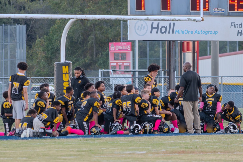 A football team outside under a goal post.  The players are wearing black and gold uniforms listening to a coach.