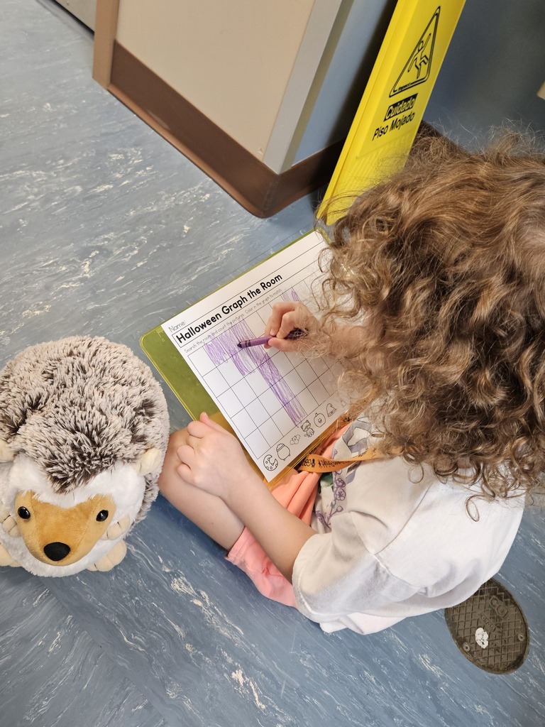 Kindergarten student working hard alongside Hedgie the Hedgehog stuffed animal.