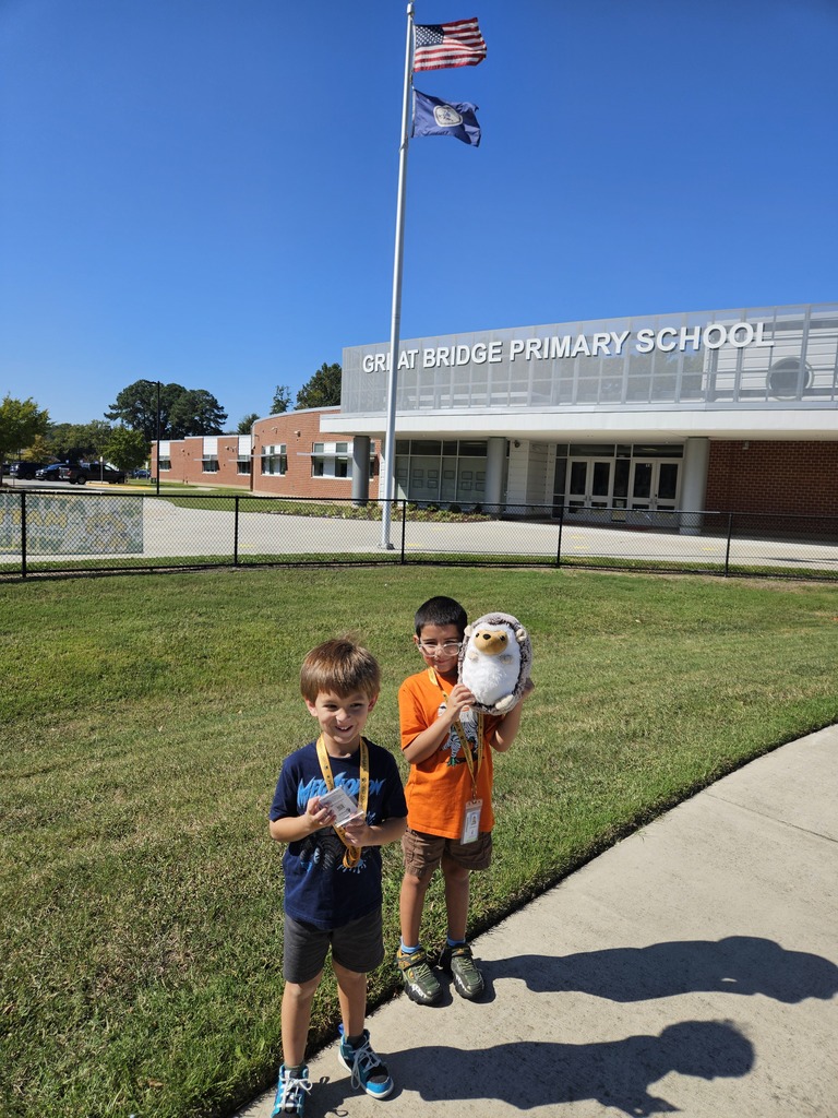 Students holding Hedgie the Hedgehog stuffed animal proudly in front of the school.