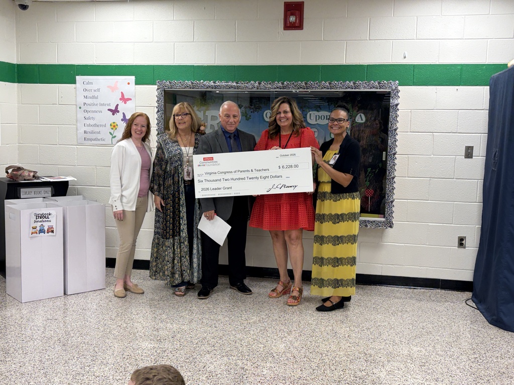 Five adults stand together in a school hallway posing with a large ceremonial check presented by JCPenney Communities Foundation. The check is made out to the Virginia Congress of Parents & Teachers for $6,228.00 as a 2026 Leader Grant. They are standing in front of a bulletin display, with white donation bins on the left.   
