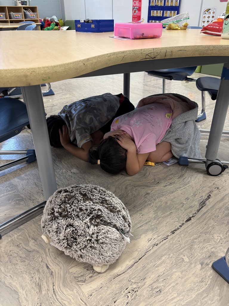 Two children lying on a classroom floor with a beanbag chair nearby and a table above.