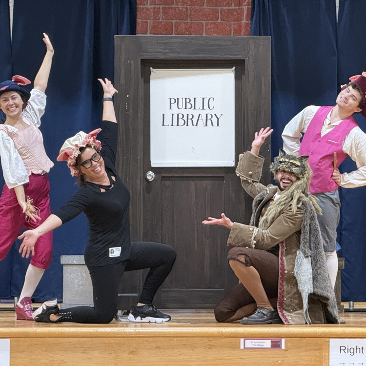 Four performers smiling around a door and a public library sign.