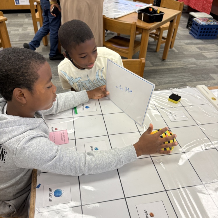 two students work together to code their bee bit on a mat.