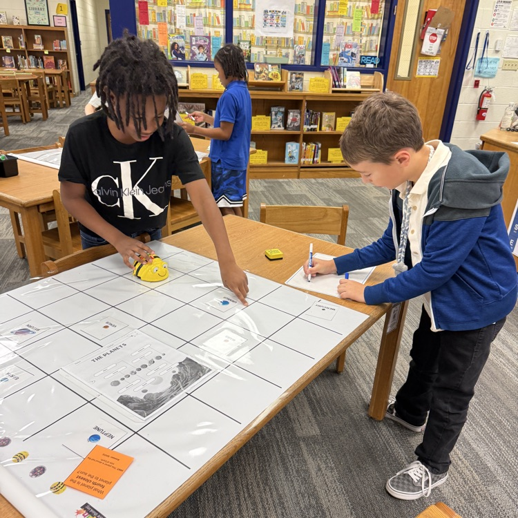 two students work together to code their bee bit on a mat.