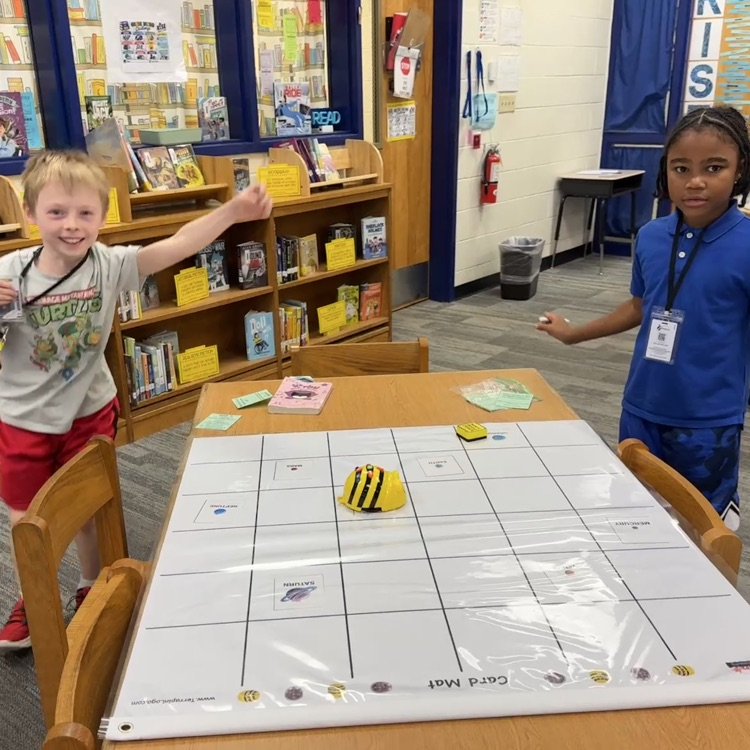 Two students celebrating next to their bee bot on the mat.