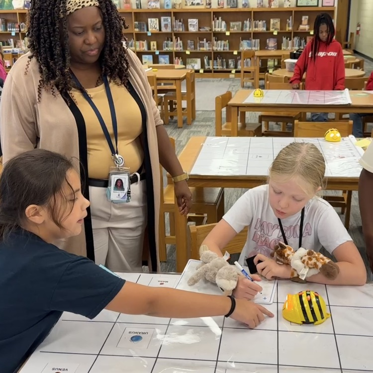 two students and Mrs. Young work together to code their bee bit on a mat.
