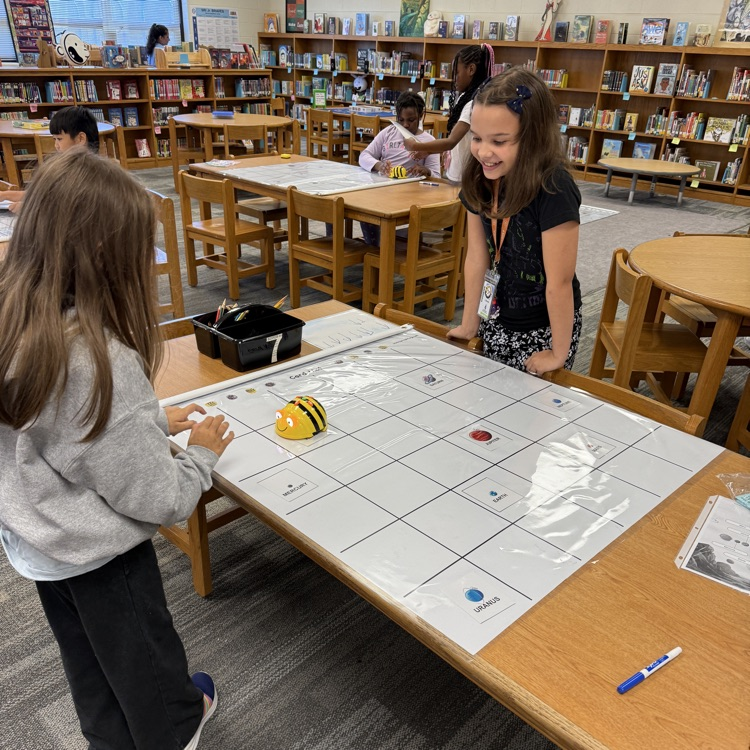 two students work together to code their bee bit on a mat.