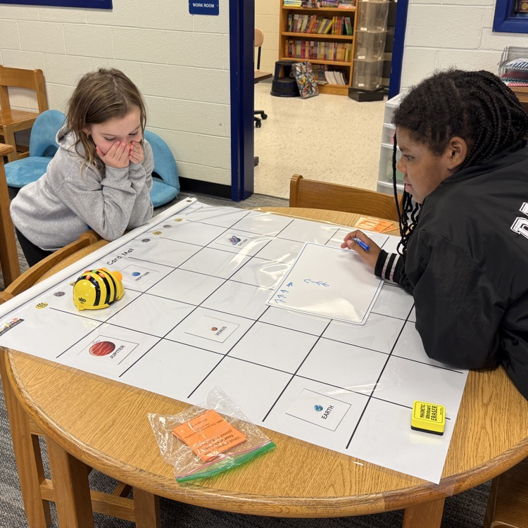 two students work together to code their bee bit on a mat.