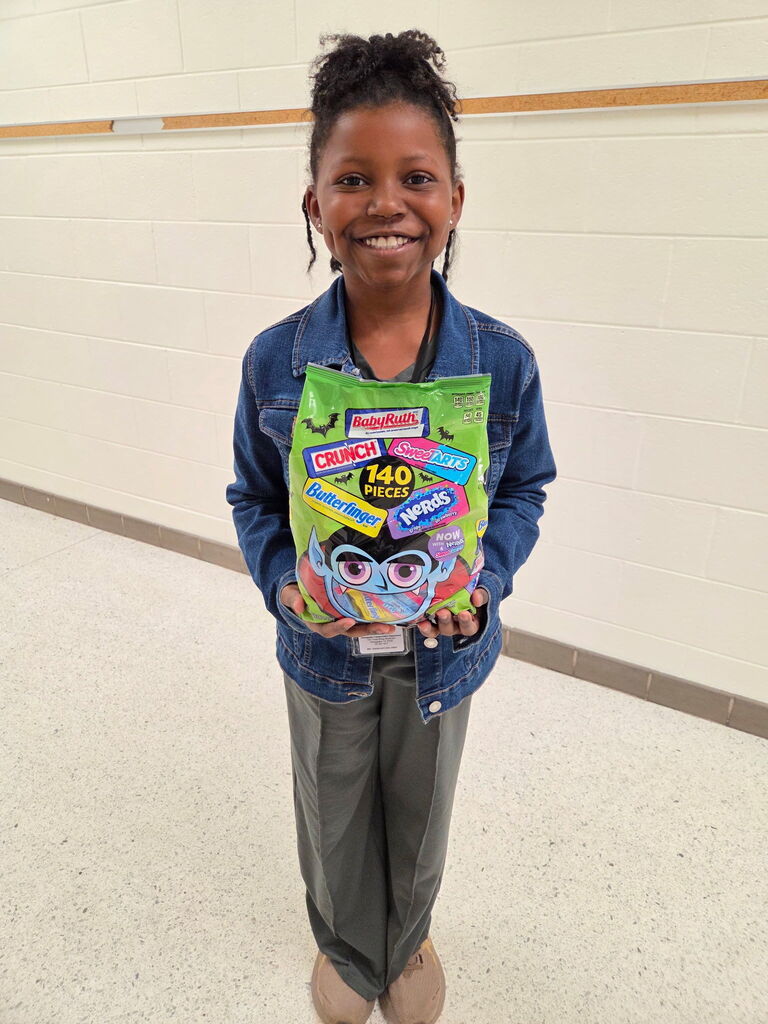 Child holds a colorful bag of candies in front of a white wall in a hallway.