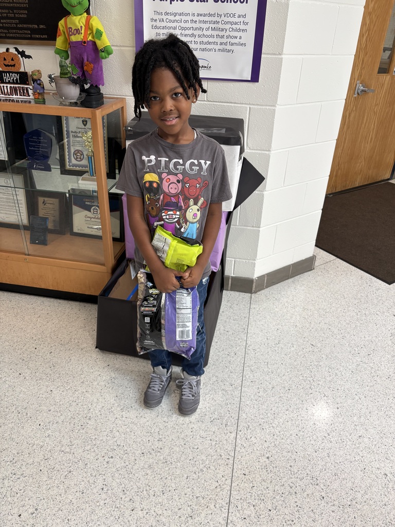 A child stands in a hallway holding a bag, wearing a gray t-shirt, and has a smile.