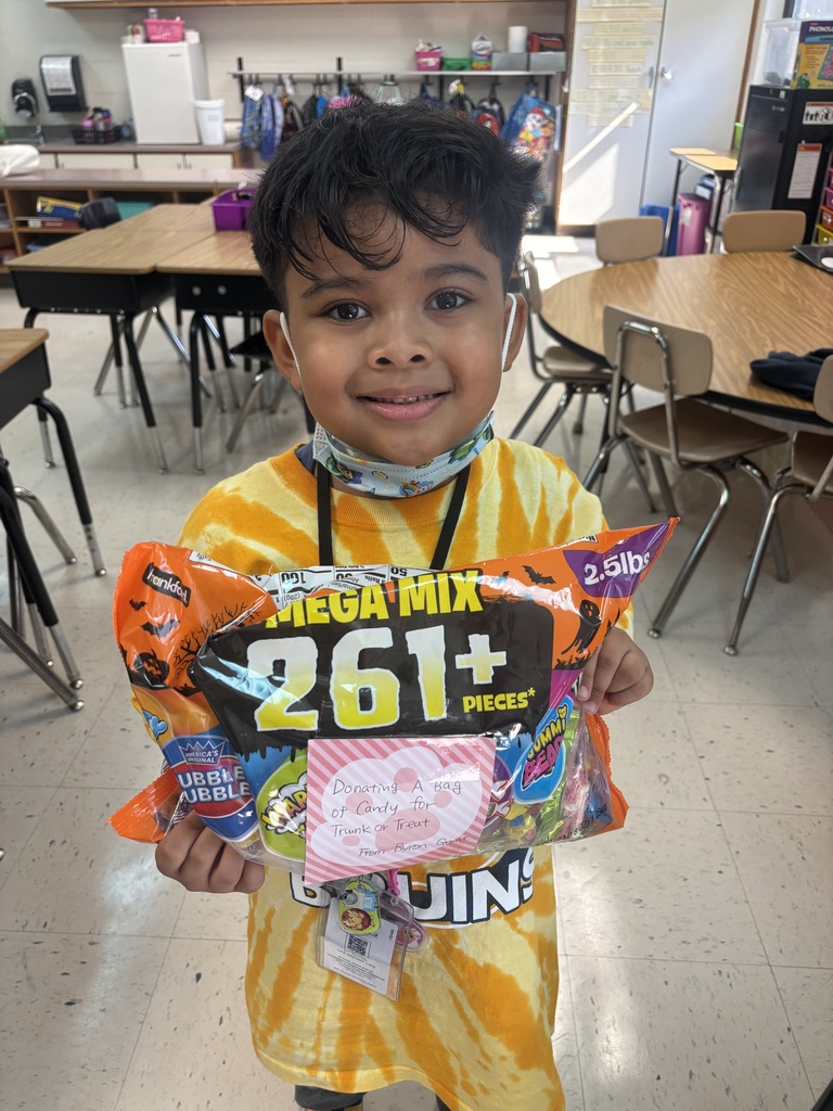 Child in yellow shirt smiling, holding a bag of candies and a sticker with a number.