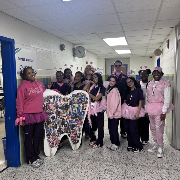 A group of students wearing pink outfits and tutus stand in a hallway with a tooth.