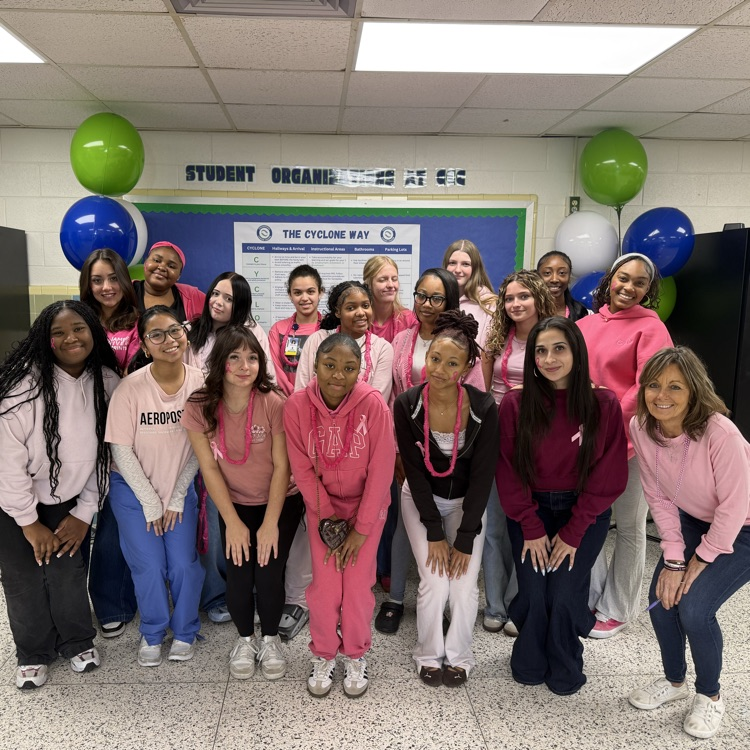 A classroom with balloons, a bulletin board, and students in pink shirts posing for a group photo.