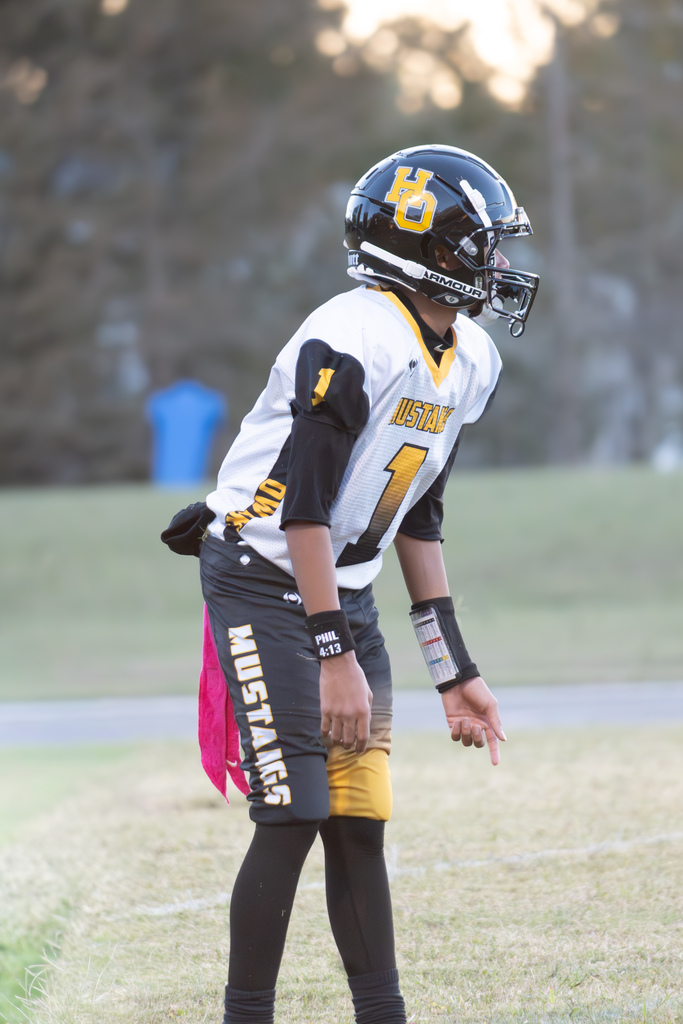 A football player is standing on a field wearing yellow, black and white uniform with Mustangs and the number one on it.   