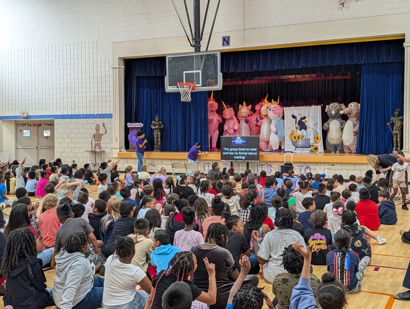 costumed staff members on stage, kids sitting on the floor