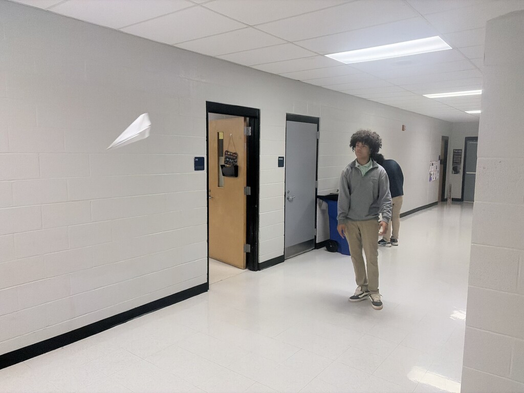 A student watching his airplane fly down the hall. 
