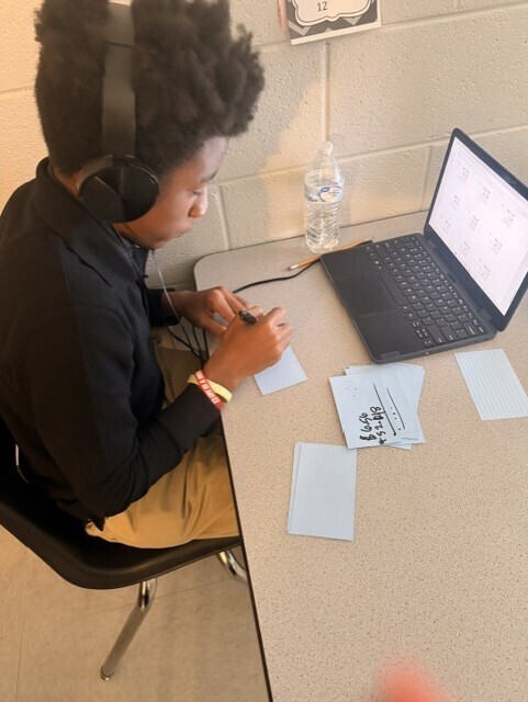 A student working on math problems for his group's game. 
