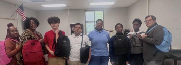 TLC students, Linde representative Tia Hill and TLC director David Spencer along with backpacks and school supplies donated by Linde's Moore Air Separation Unit.