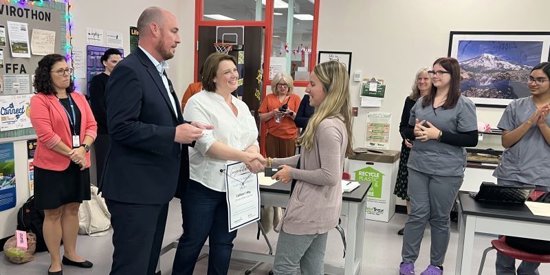 A group of adults presenting an award to a teacher in a classroom