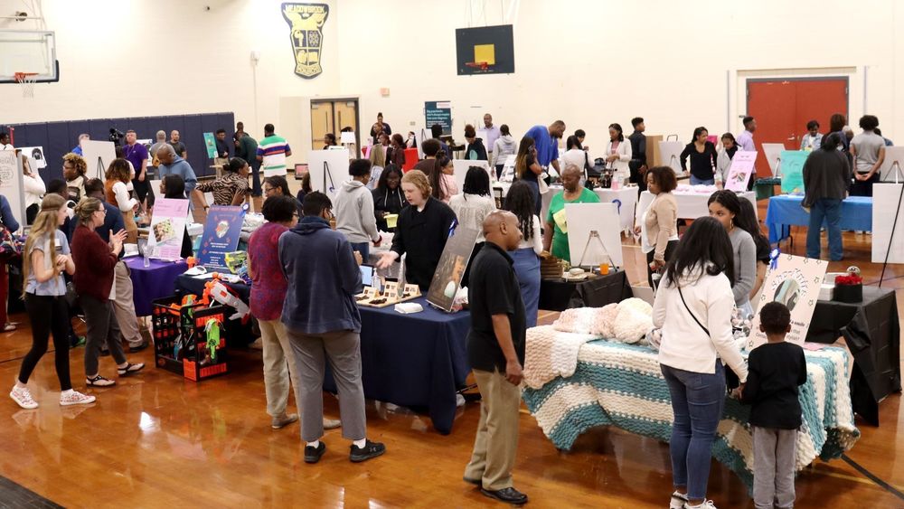 A school gym full of people and tables in the Student Business Expo