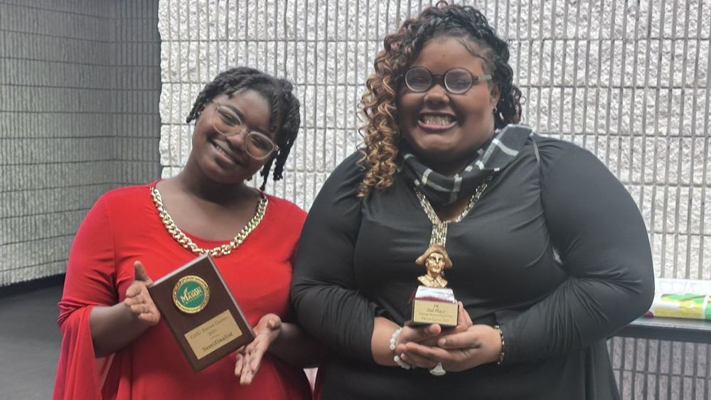 Two students holding trophies and smiling