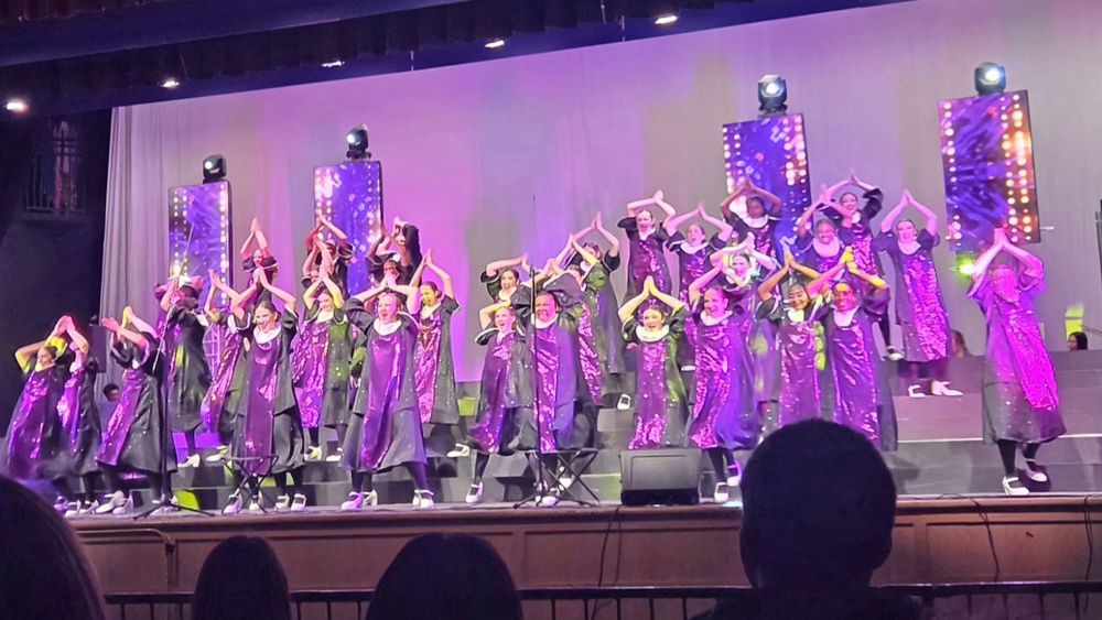 A group of students in purple outfits dancing on stage
