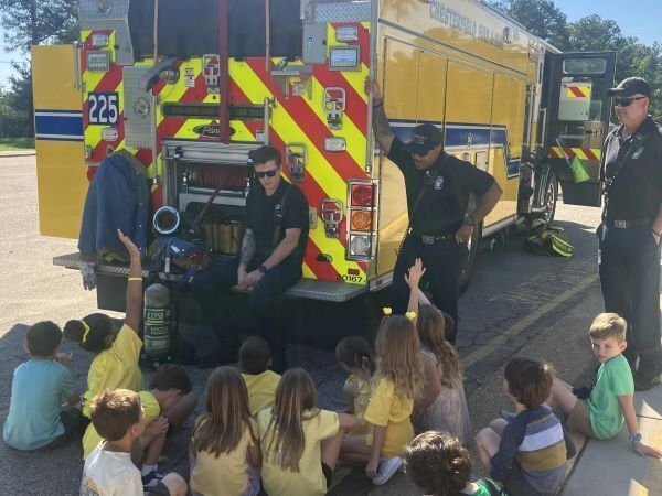 Students raising hands in front of a fire truck